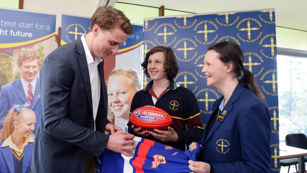 GOOD SPORT: Jordan Roughead signs Western Bulldogs memorabilia for Damascus College students Tim Collins and Jess Rowse. Picture: Kate Healy