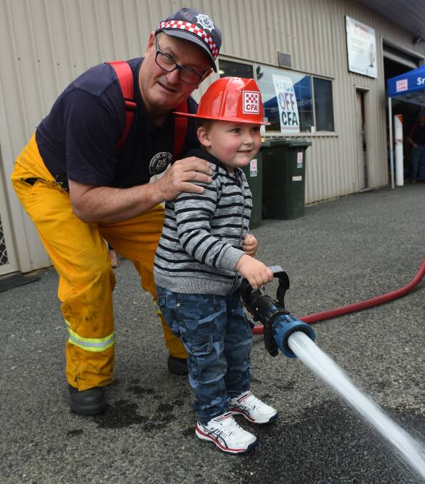 TURNING UP THE HEAT: Smythesdale CFA member Simon Turner shows Lochie Howlett, 3, how to use the hose. Picture: Lachlan Bence.