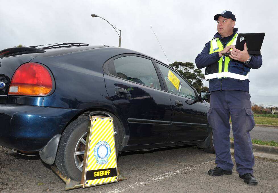 CAUGHT RED HANDED: Senior Sheriff's Officer Andrew Bott along with Ballarat police blocked off Wendouree's Norman Street on Thursday to catch fine evaders, including the owner of this clamped Ford. Picture: Lachlan Bence 