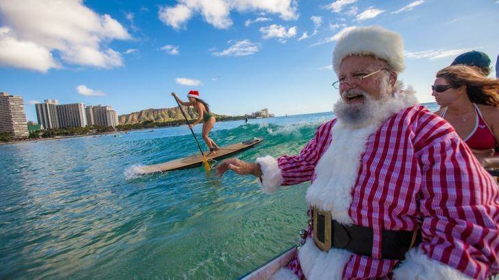 Santa arrives by outrigger canoe at the Outrigger Waikiki Beach Resort in Hawaii.