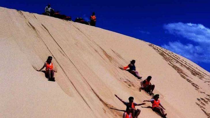Sand boarding down the dunes of the Worimi conservation lands. Photo: Sand Dune Adventures