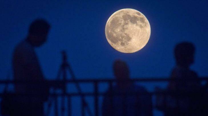 People stand and look at the Supermoon phenomenon from a bridge over 42nd St. in the Manhattan borough of New York July 11, 2014. Occurring when a full moon or new moon coincides with the closest approach the moon makes to the Earth, the Supermoon results in a larger-than-usual appearance of the lunar disk.          REUTERS/Carlo Allegri (UNITED STATES - Tags: SOCIETY CITYSCAPE)