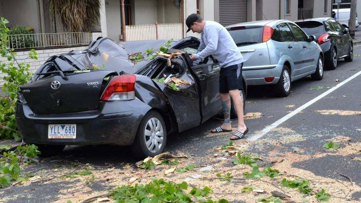 A man inspects a storm-damaged car in Carlton. Photo: Joe Armao