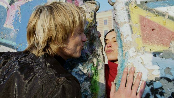 A couple blow a kiss to each other through the mural-covered remains of the Berlin Wall.