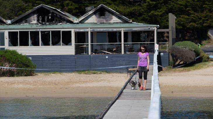 A woman walks her dog on the pier in front of "The Baths", the morning after fire gutted the popular function and wedding centre. Photo: Jason South