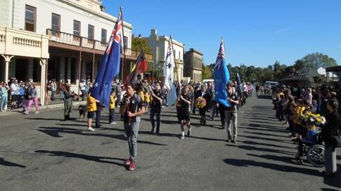 Members of the Clunes Football & Netball Club carry the flags whist leading the March down Fraser Street, Clunes. PICTURE: MICHAEL CHESIRE