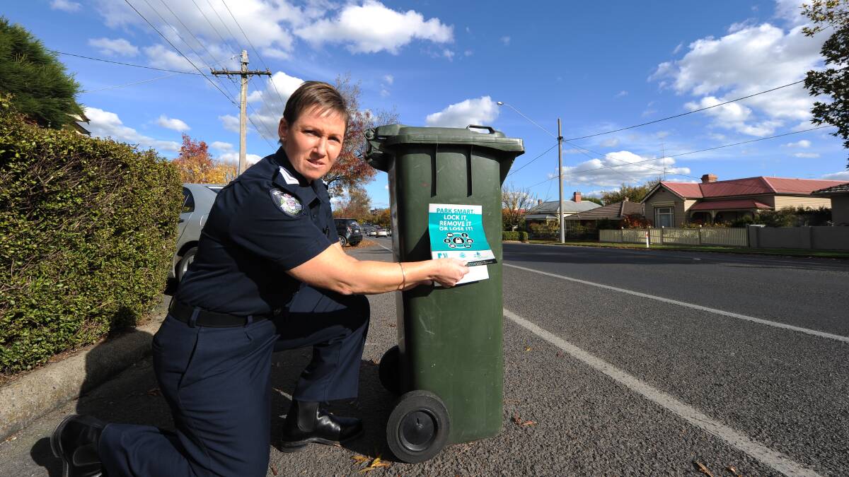 Senior Constable Janine Walker puts a sticker on a rubbish bin to warn residents about an increase in thefts from vehicles in the area.