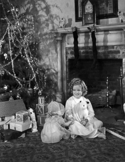 Shirley Temple sitting by her Christmas tree with presents from 20th Century Fox and a decorated Christmas tree in 1936. Picture: Getty Images