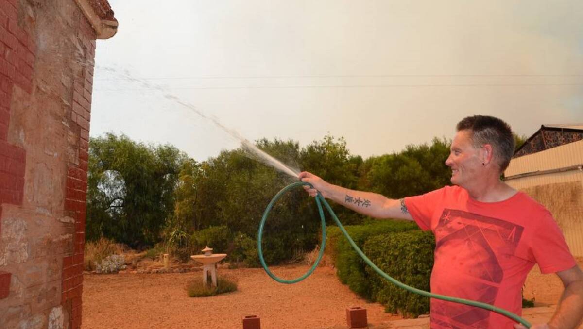Telowie resident Derek Morris hoses down his house, with smoke visible in the background.