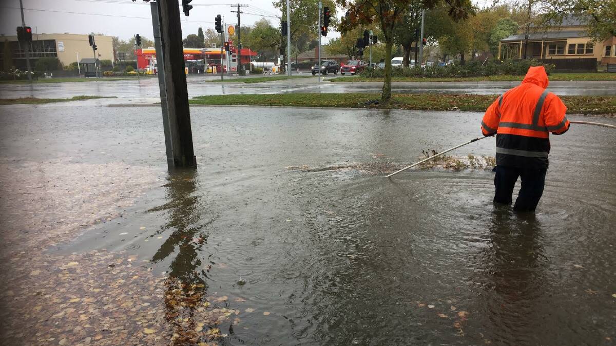 A council worker trying to unblock drains at the corner of Pleasant and Sturt streets. Photo: Peter Blenkiron.