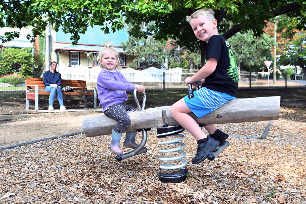 Creswick mum Kate Mackie takes a seat on the new park bench while her children Zarah Geljon, age two, and Elliot Geljon, six, play in the Magic Pudding Playground. Picture by Kate Healy