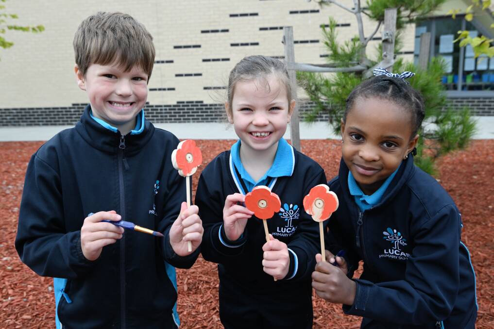 Lucas grade one pupils Mac, Eloise and Christel show their red poppies in progress, painted near the school's lone pine tree ahead of Anzac Day 2024. Picture by Kate Healy