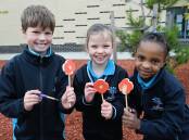 Lucas grade one pupils Mac, Eloise and Christel show their red poppies in progress, painted near the school's lone pine tree ahead of Anzac Day 2024. Picture by Kate Healy