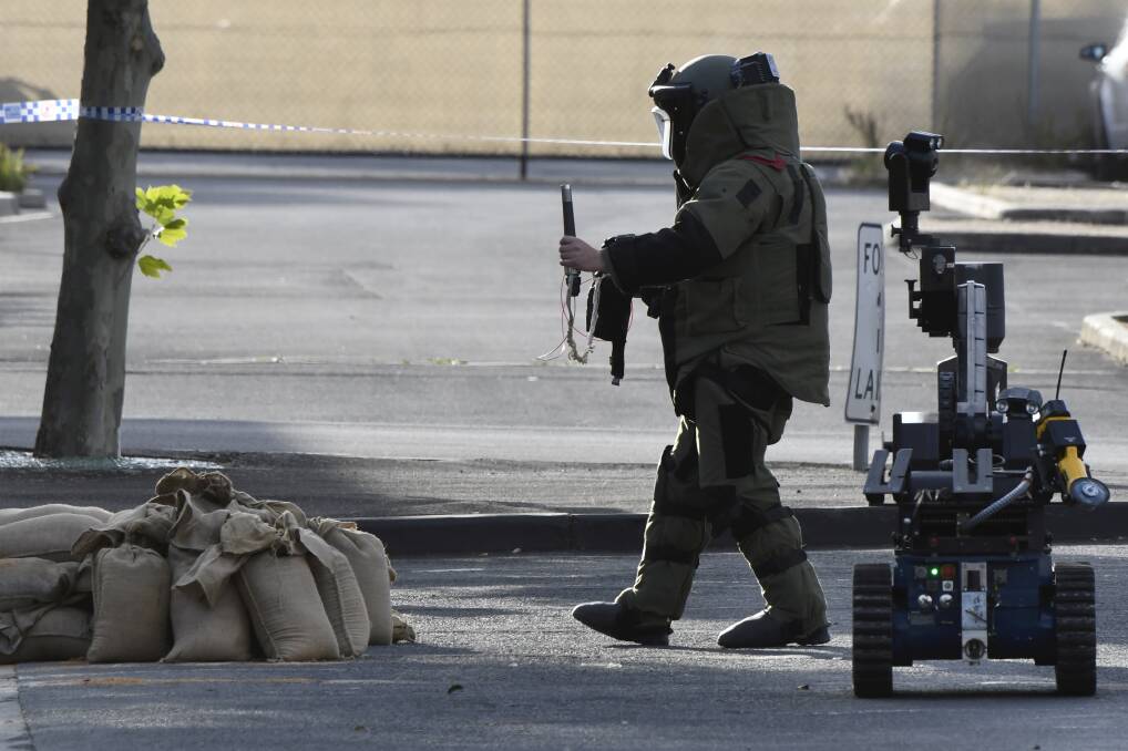 A police officer in explosives safety gear approaches the item in the sandbags with a bomb disposal robot. Picture: Lachlan Bence
