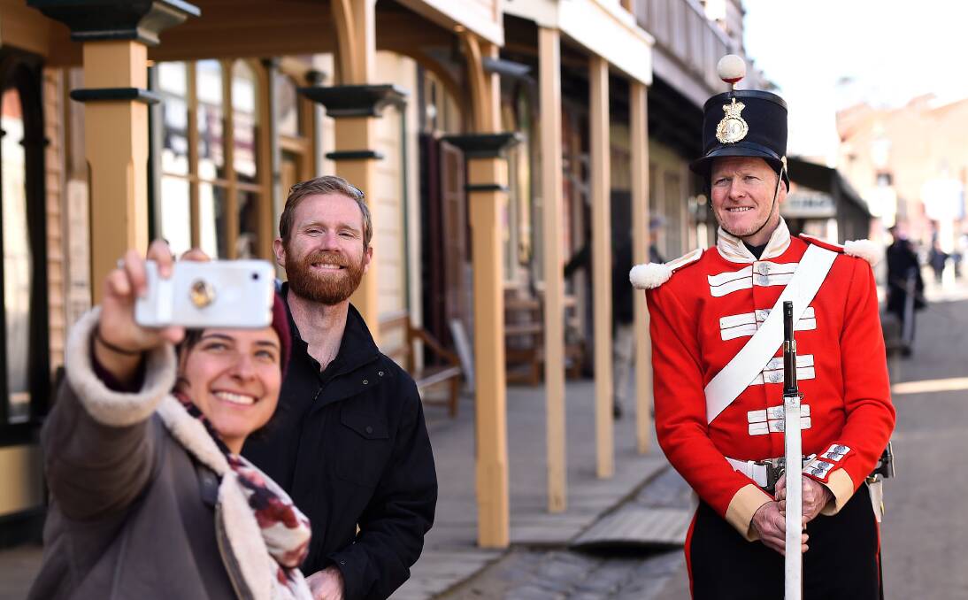 Rebuilding: Sovereign Hill trooper Michael Durham takes a socially distanced photo with tourists. Picture: Adam Trafford.