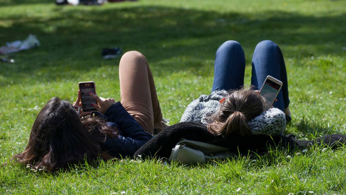 Two girls lying in the grass in a park sending and reading text messages and not 
 speaking with each other on a sunny day. Picture: AP