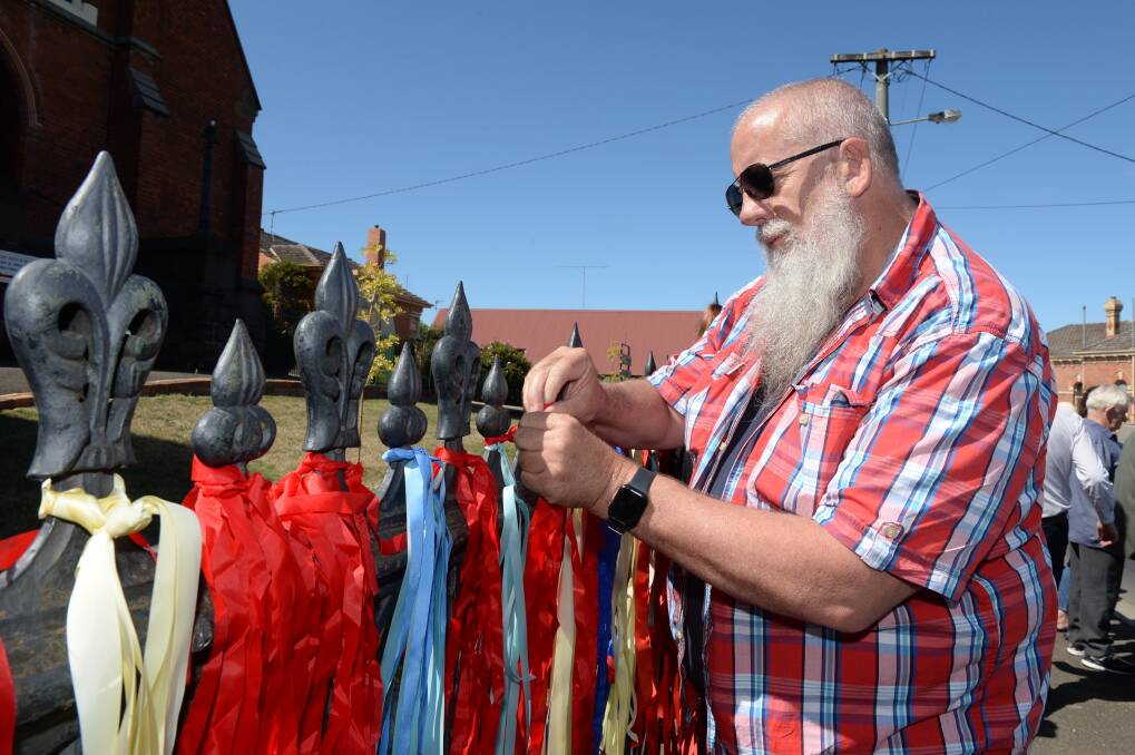 SYMBOLIC: Andrew Aiden places red ribbons on the fence outside St Paul's Anglican Church in Bakery Hill on Saturday in support of abuse victims. Picture: Kate Healy