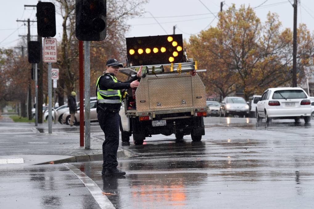 It's a wet job but someone has to do it. Police direct traffic after the lights went out at the corner of Sturt and Drummond Street on Wednesday. Picture: Kate Healy