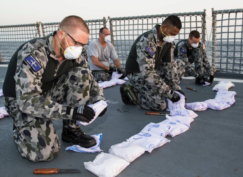 Able Seaman Maritime Logistics Support Operations Benjamin Lindsay (left) removes the outer packaging of suspected narcotics seized by HMAS Ballarat prior to its disposal. Picture: Australian Defence Force