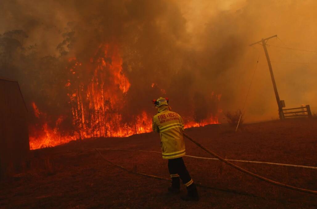 Firefighters protect property from a bushfire on Lakes Way, north of Forster near the junction of the Pacific Highway on Friday. Photo: Dean Sewell