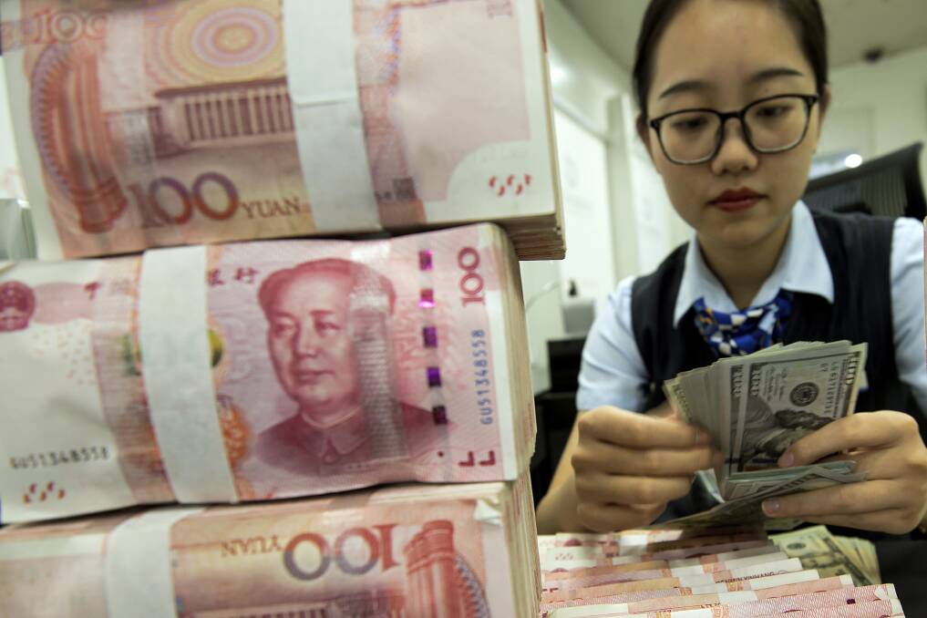 Currency woes: A bank employee counts US dollar banknotes next to stack of 100 Chinese yuan notes at a bank outlet in Hai'an in eastern China. China's yuan fell further this week against the US dollar, fuelling fears of increasing global damage from Beijing's trade war with Donald Trump. Photo: AP