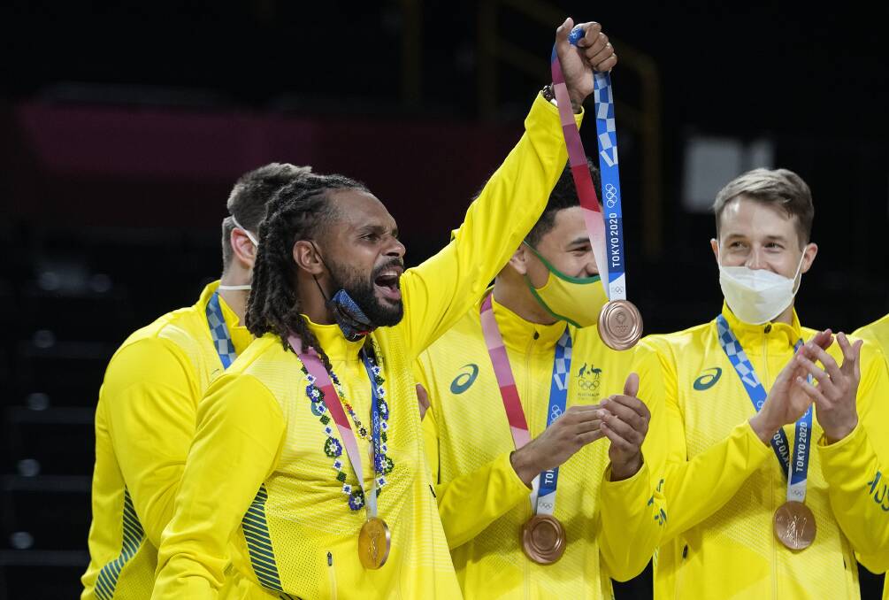 Former Ballarat Miner Nathan Sobey, right, watches as Patty Mills hoists a bronze medal into the air for injured teammate Aron Baynes. Picture: AP/Eric Gay