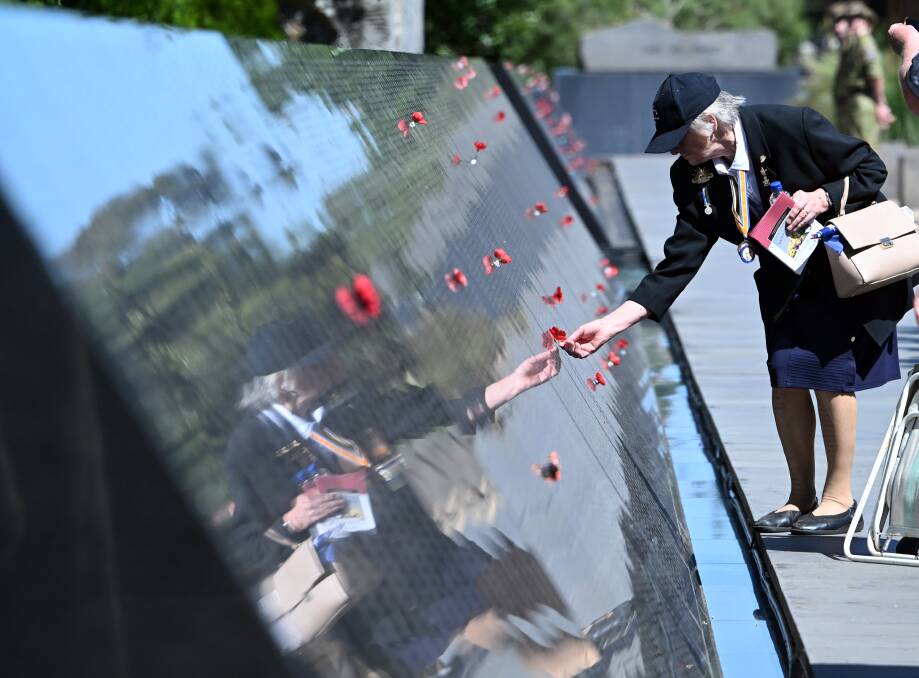 A woman places a poppy on one of the 36,400 names etched into the Australian Ex-Prisoners of War Memorial which marked its 20th anniversary on Sunday. Picture by Kate Healy