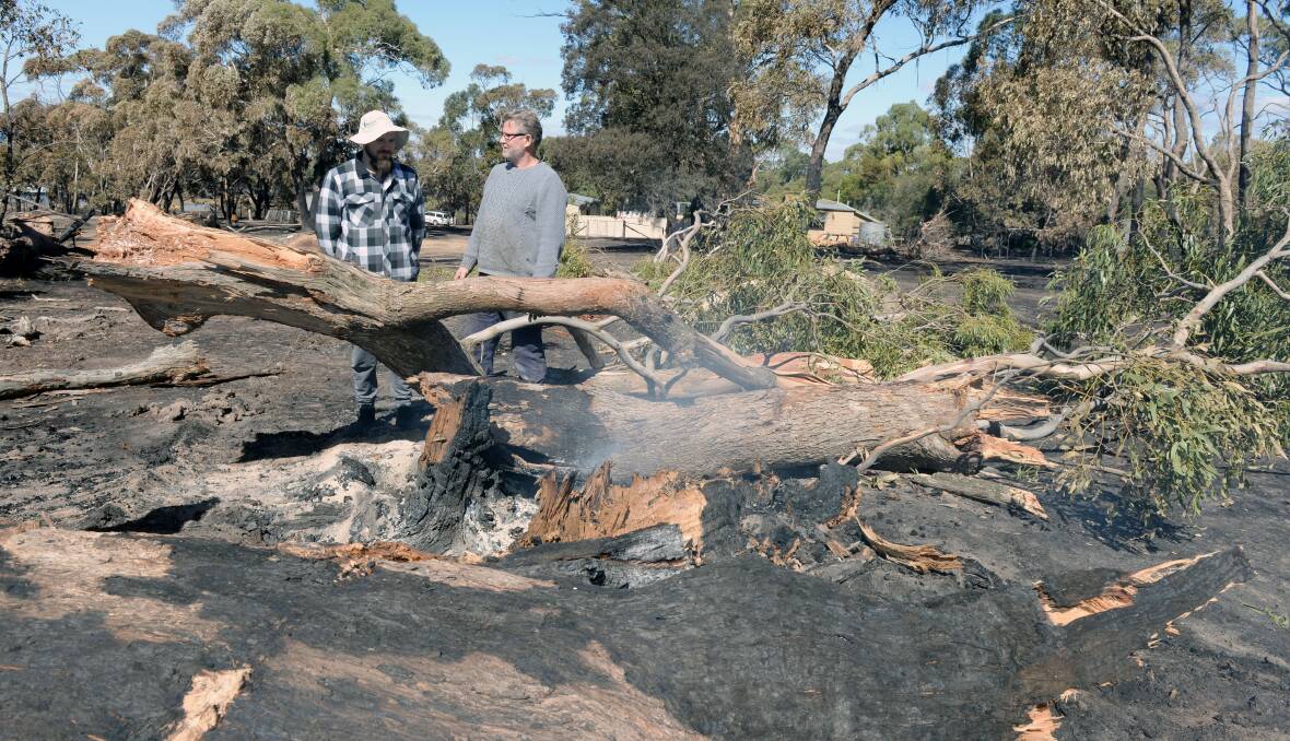 SMOULDERING: Luke Dower and his dad Evan near a tree that was still smoking more than 72 hours after the Bunkers Hill bushfire. They managed to save their house from the inferno but lost several sheds. Picture: Kate Healy