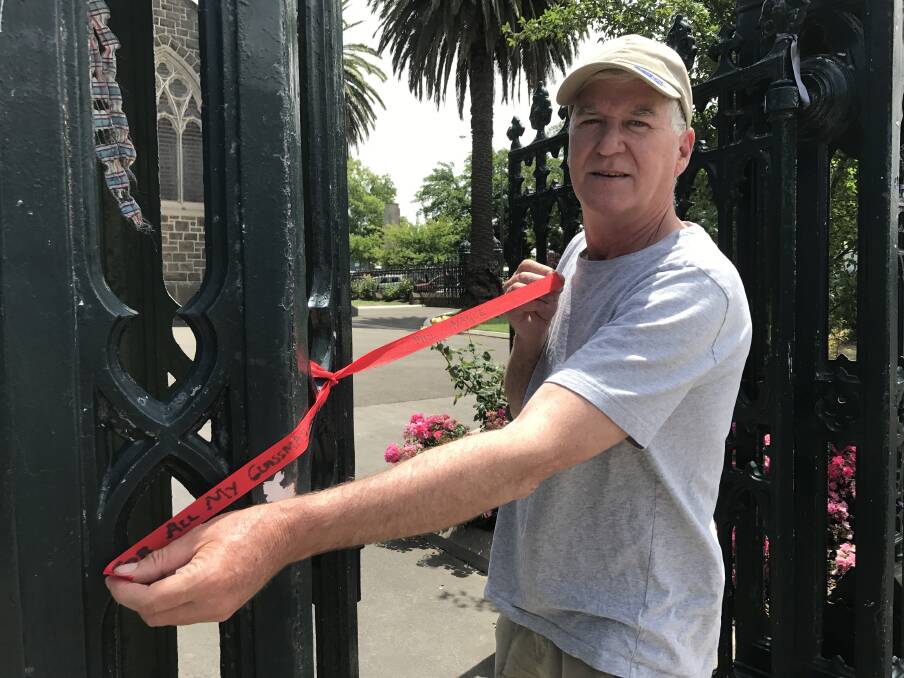 SURVIVOR: Phil Nagle ties a new ribbon to the fence outside St Patrick's Cathedral, before parishioners removed the ribbons and placed them in a memorial garden. Picture: Michelle Smith