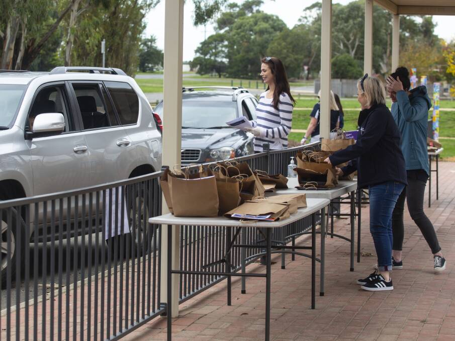QUEUE: Teachers hand out learning packs to students and their parents waiting in cars at Lumen Christi Primary School. 