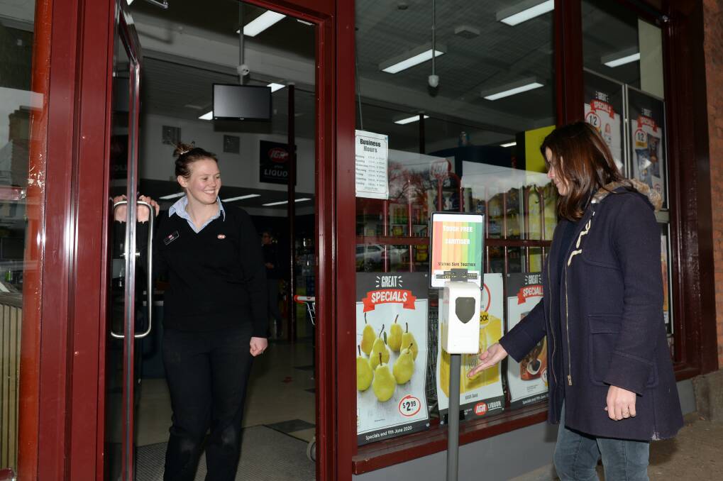SAFETY: Clunes IGA assistant manager Jess Hill helps a customer use a new automated hand sanitiser machine outside the store. 