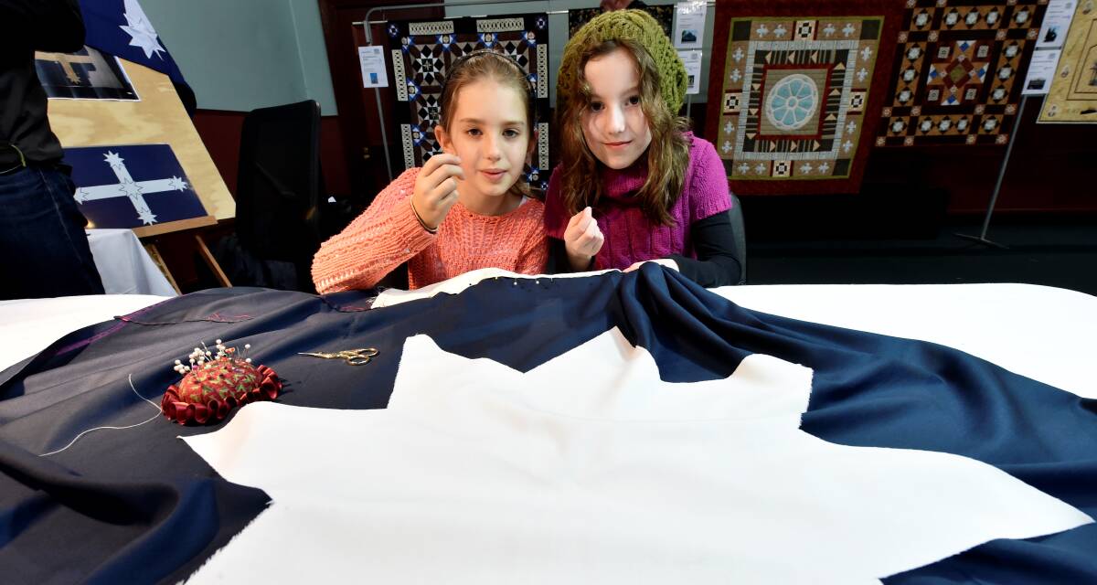 Remi Currie and Anastasia Parker take part in sewing the replica Eureka Flag as part of the Rug Up Market.