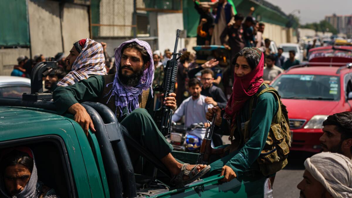 Afghans march down the street carrying the flag of the Islamic Republic of Afghanistan, despite the presence of Taliban fighters around them, in Kabul on Thursday. Picture: Getty Images