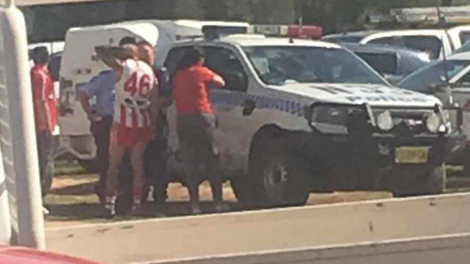QUESTIONS: Maksymow, pictured wearing his football gear, is spoken to by officers at Walbundrie on Saturday. He agreed to be arrested at full time but fled the ground.
