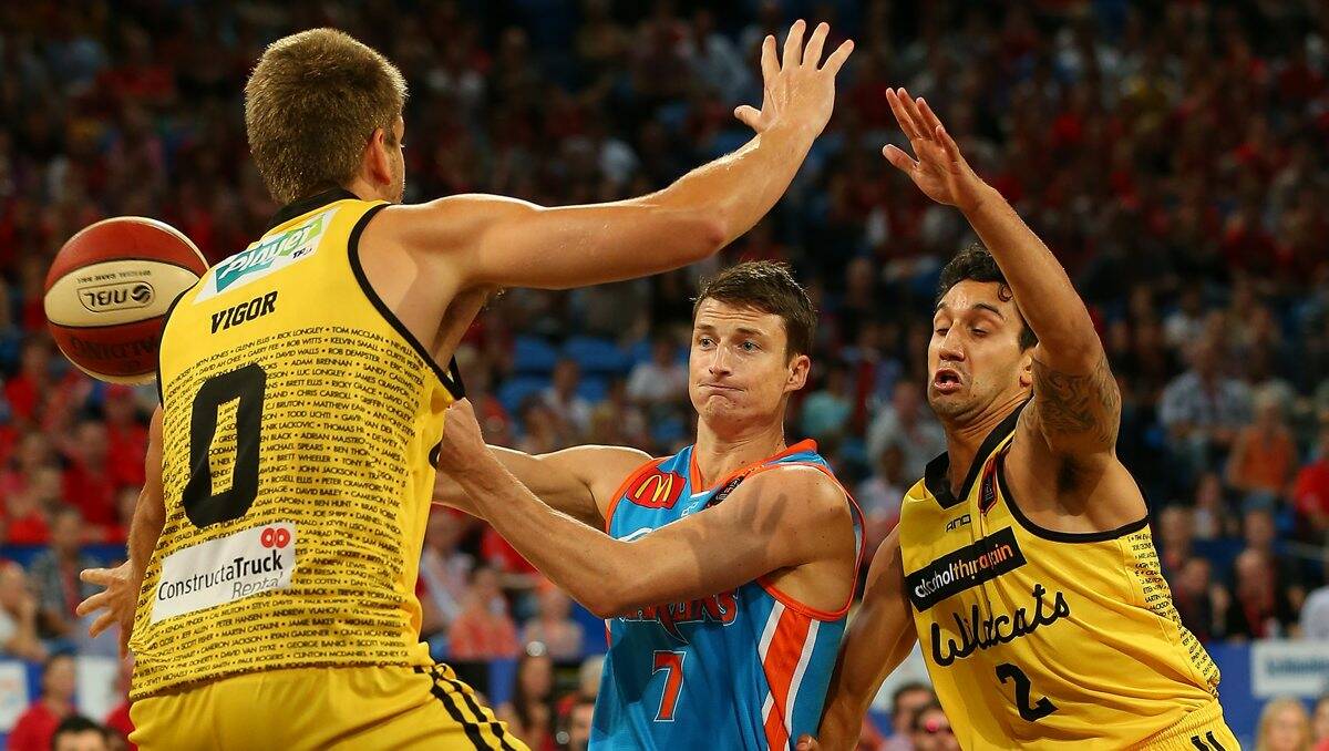 Shaun Bruce of the Taipans passes the ball against Michael Vigor and Kyle Armour of the Wildcats.